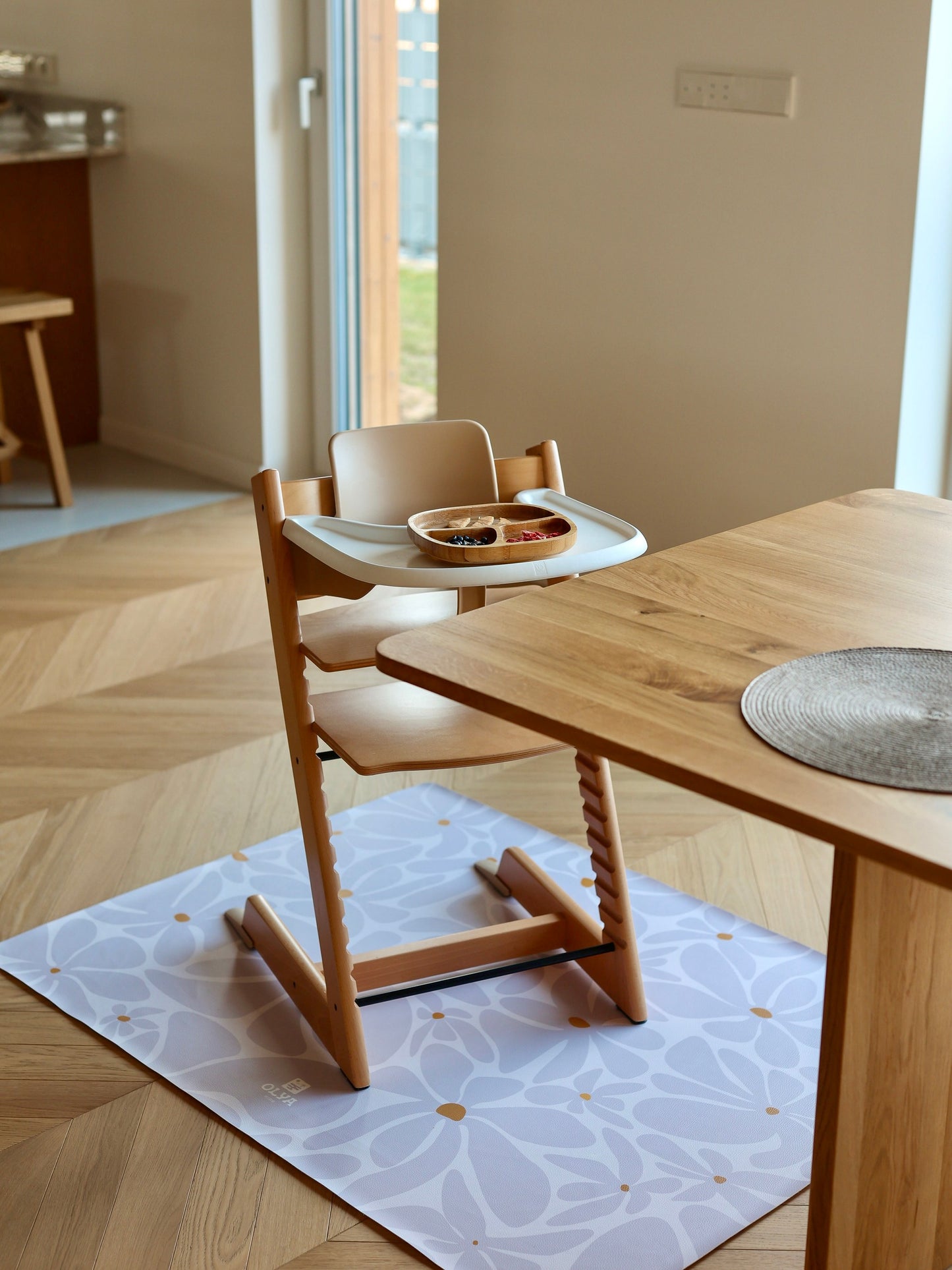 Tapis de repas bébé imperméable installé sous une chaise haute en bois naturel