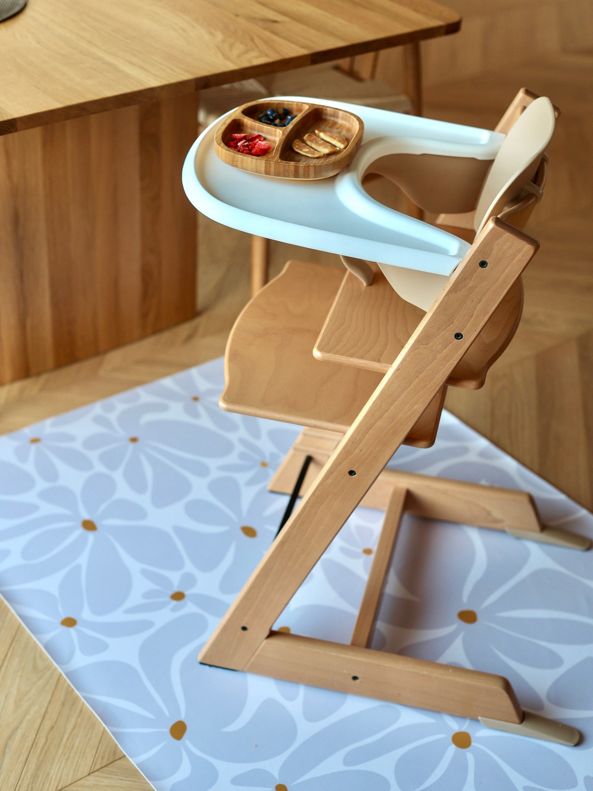 Détail du tapis de protection imperméable Daisy Lavender sous une chaise haute en bois